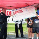 $16,080 check made by Shoney's being handed to a police officer.